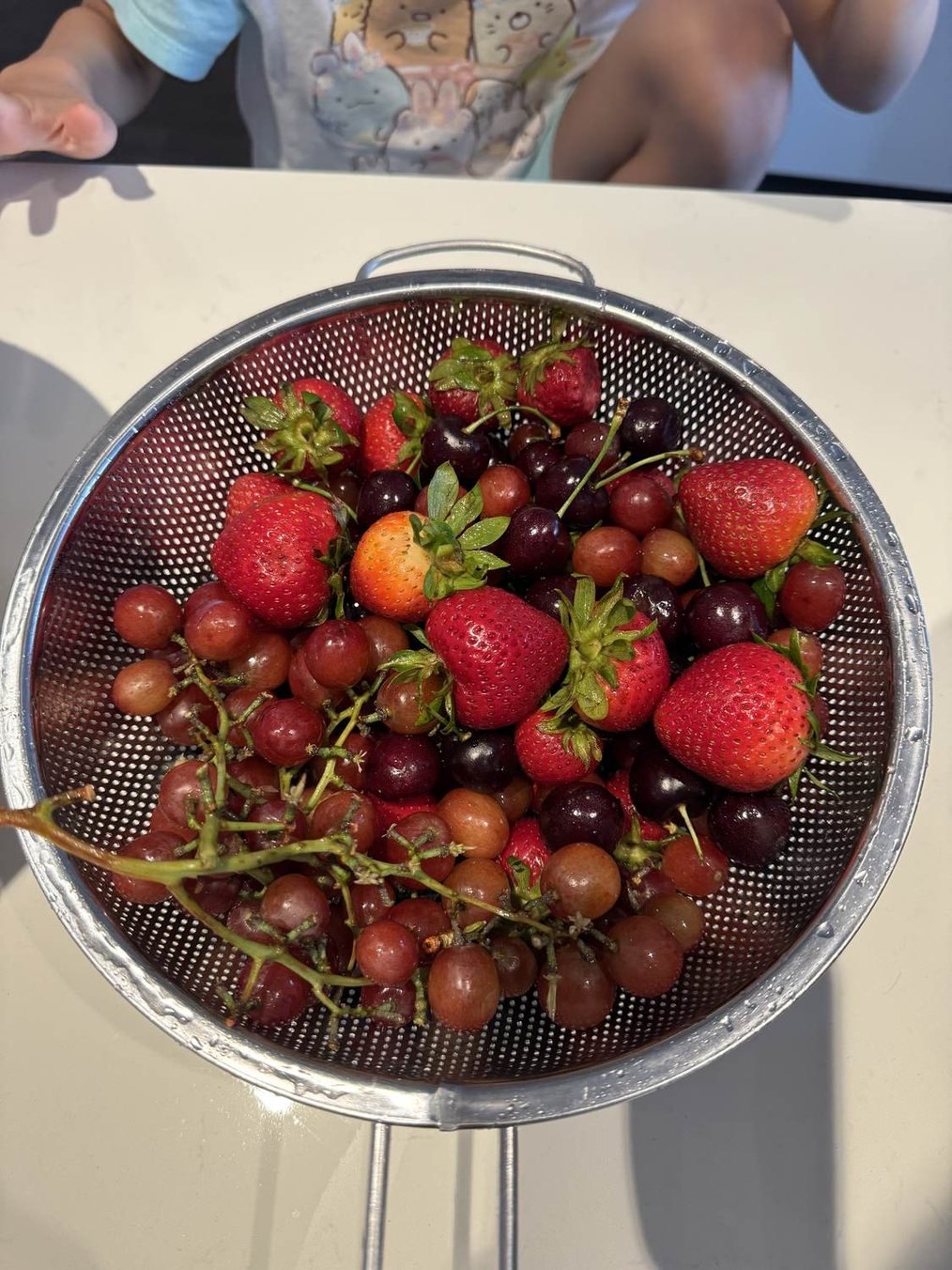 A colander of fresh strawberries, cherries and grapes